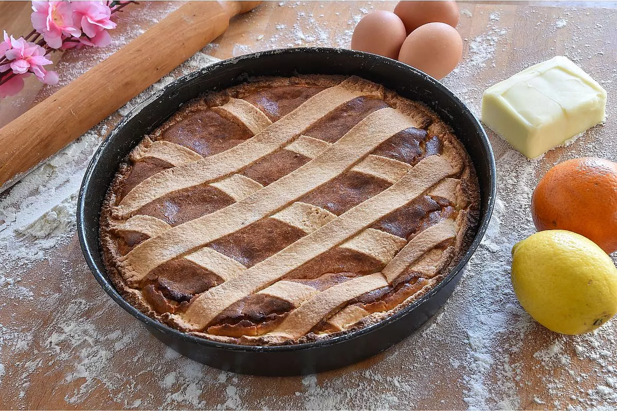 Pastiera napoletana su un tavolo, con ingredienti e mattarello