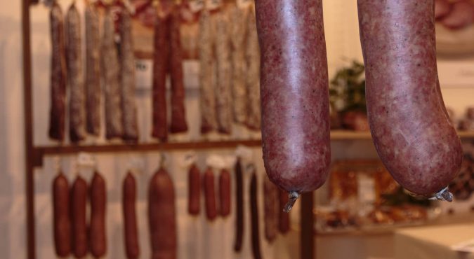 Closeup of Sausages and Variety of Raw Meat and sausages in background inside Butcher Shop