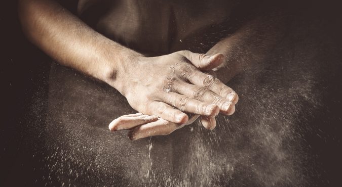 Unrecognizable cook clapping hands with flour while making dough.