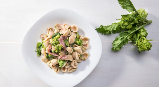 Traditional dish of Apulia region pasta Orecchiette with turnip greens and salted anchovies, top view, white wooden background